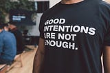 This is a photo of a person wearing a tshirt that says “good intentions are not enough”