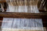 A wooden loom is shown with threads of material on it.