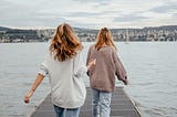 back of two girls in sweaters walking towards end of dock