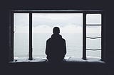 a lone man, sitting on a windowsill, facing the ocean, seen from behind.