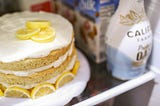 A lemon layer cake on a shelf in a fridge next to creamer