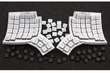 An official product image of the Glove80. It is a split keyboard with two wireless halfs, with mirrored layouts. The keyboard consists of a curved cluster for each thumb with two rows of three keys, and a curved main board with six rows and six colums, holding 34 keys for side. In total it has 80 keys. The curvature and position of each column of keys follows the motion of the fingertip as the fingers curl and uncurl.