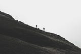 Two people and one dog climbing a steep mountain