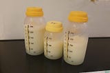 A photo of three milk bottles with varying amounts of milk in them, the size of two of the bottles is 250ml and the other bottle is 150ml, all the bottles have yellow lids and they have measurement markings up their side, the milk inside them has separated slightly with thicker cream on the top and greener/yellowy water near the bottom