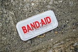 Close up of Band-Aid container resting on concrete ground.