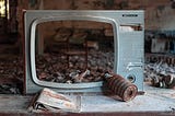 A broken TV sitting amidst other debris in a destroyed building, in some dystopian landscape.