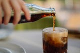 Someone pouring cola from a glass bottle to a drinking glass