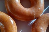 a close-up image of freshly glazed Krispy Kreme donuts in a box. Yum!