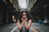 A woman with a straight face standing in the middle of an empty road.