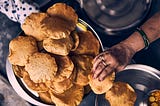 A woman’s hand that is picking up puris served on a plate.