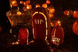 Three carved pumpkings, lit up at night. The middle one says RIP.