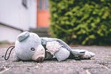 A child’s teddy bear lying on the ground. A front door in the foreground.