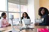 Three women of color sitting at a table with computers.