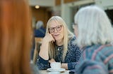 Two women with gray hair sit with a coffee cup between them.
