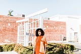 A confident woman wearing a bold, eclectic outfit that showcases her unique personal style, standing against a backdrop of conventional brick building.