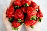 Ldown on a person’s hands together side by side holding as many strawberries as they can.