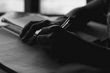 A black and white photo of a person’s hands holding a pen and writing in a notebook.