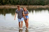 A man and woman holding hands as they walk across the water.