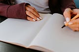 Hands writing in a journal. The pages are blank.