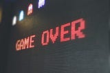 Photo of a computer monitor from a side angle. The monitor reads “GAME OVER” in bold, red letters. 4 small Pacman ghosts are above it.