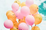 Pink and orange balloons in a bunch with happy and sad faces on them