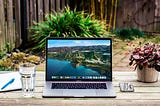 Picture of a laptop on a wooden desk outside in a beautiful location.