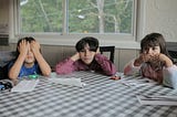 Three kids at a kitchen table making see, hear, and taste gestures.
