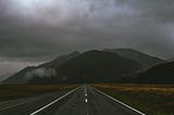 A photo of a dark highway leading toward dark mountains.