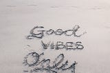 The words ‘Good Vibes Only’ drawn in the sand of a beach.