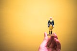A hand holding a George Washington figurine against a yellow background