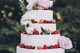 Layer cake with white frosting, fresh fruit, and fresh flowers