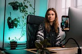 A woman poses for a video recording while seated at a content creation setup.