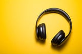 Black on-ear headphones on a warm yellow surface.