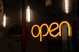 A yellow sign that says OPEN, against a dark background with some lightbulbs