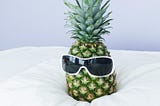 A pineapple, sitting on a bed, with sunglasses on!