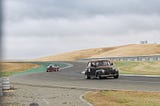The 1941 Ford Coupe coming out of a curve on the racetrack, followed by a pickup truck.