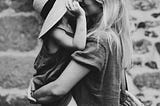 Mother holding her daughter in her arms, tenderly kissing her under her hat.