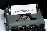 Close-up of a vintage typewriter with a sheet of paper that has the word “INVESTIGATION” typed in bold capital letters.
