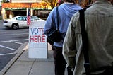 People standing in line on a sidewalk waiting to vote.