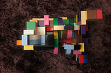 Arte em lego, com peças multicoloridas e multiformas, contra um fundo felpudo em tons de roxo.