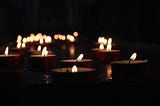 Lots of tea light candles, lit against a dark background