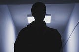 Photo of the silhouette of a person in a dimly lit corridor