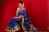 A woman wearing a navy blue saree background red color