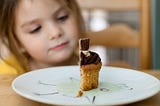 Picture of a child looking at a quarter of a cup cake on a plate