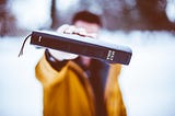 A man in a yellow coat holding a Holy Bible out toward the camera