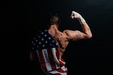 A guy half naked, half draped in the American flag, flexing his muscles.