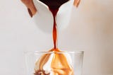 a cup of espresso being poured over vanilla ice cream that’s in a clear glass