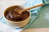 White dessert bowl filled with a chocolate mousse type pudding with sprinkles of orange zest. A wooden spoon has been placed in bowl for serving