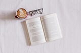 An open book, a pair of glasses, and a cup of coffee on top of a white background.