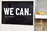 A black tile on a white wall with the words " we can. Just imagine" on it.